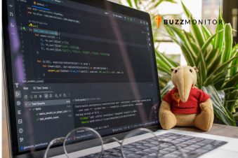 Notebook con código abierto en IDE junto a peluche de Buzzmonitor, representando el uso de IA para el monitoreo de marca en redes sociales